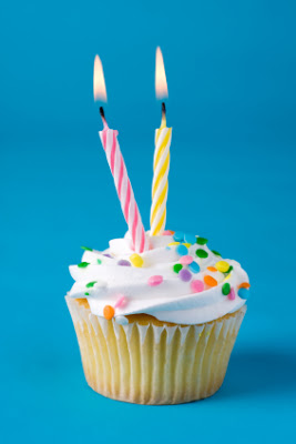 A birthday cupcake with two lighted candles.